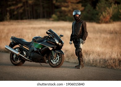 Motorcycle driver in a helmet and leather jacket stands on the road next to a sports motorcycle - Shutterstock ID 1906015840