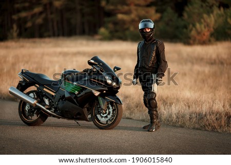 Motorcycle driver in a helmet and leather jacket stands on the road next to a sports motorcycle