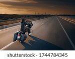 
A motorcycle driver rides alone on an asphalt highway. Biker in motion on an empty road during sunset