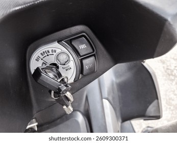 Motorcycle ignition switch with key inserted and fuel-seat control buttons visible in close-up view.