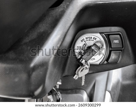 Motorcycle ignition switch with key inserted and fuel-seat control buttons visible in close-up view.