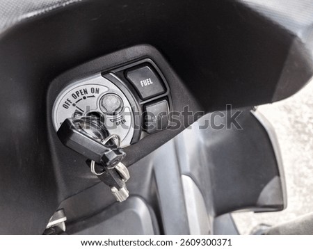 Motorcycle ignition switch with key inserted and fuel-seat control buttons visible in close-up view.