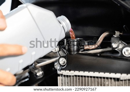 Motorcycle mechanic filling cooling system with engine coolant,pour coolant after repairing or cleaning the radiator,check liquid level in motorcycle radiator,service and maintenance concept