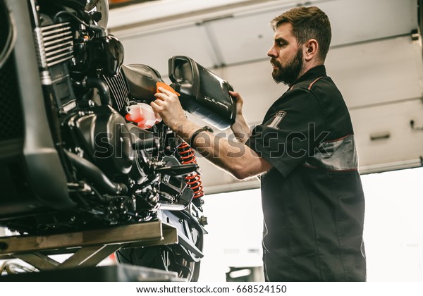 Motorcycle mechanic replacing and pouring\
fresh oil into engine at maintenance repair service station.\
Portrait of an auto mechanic putting oil in a car\
engine.