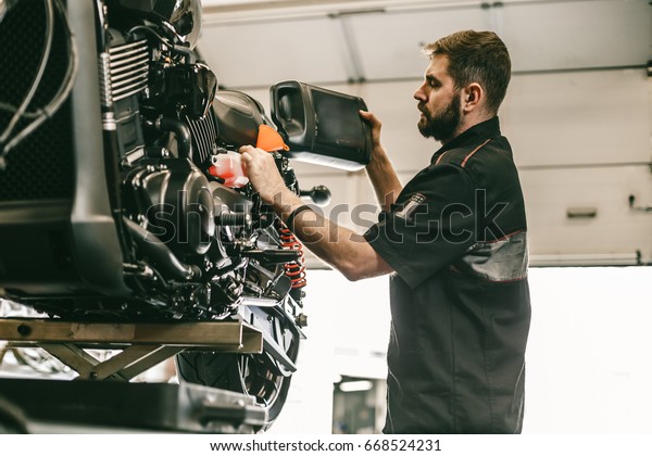 Motorcycle mechanic replacing and pouring\
fresh oil into engine at maintenance repair service station.\
Portrait of an auto mechanic putting oil in a car\
engine.