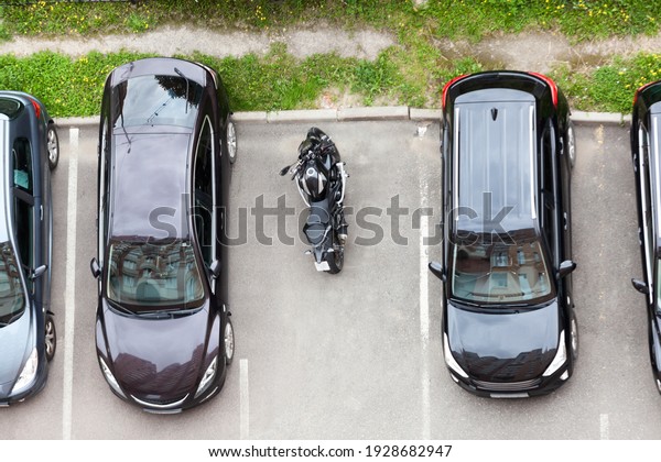 Motorcycle is parked on vehicle parking space\
between cars. Top\
view