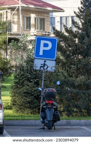 The motorcycle is parked under the parking sign for people with disabilities.
