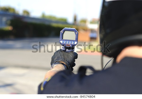 a motorcycle police officer aiming his radar gun\
a traffic.