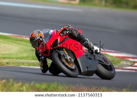 Motorcycle rider riding on a red sport bike through the corner at high speed.