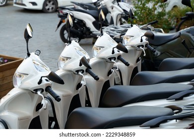 Motorcycles for rent or for sale on the city street. Lots of white scooters to ride.