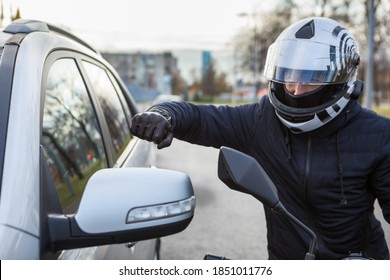 Motorcyclist beat side-view mirror of car with a fist, conflict is on the road - Shutterstock ID 1851011776