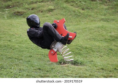 motorcyclist in black motorcycle clothing is sitting on a rocking horse on children's playground and is going crazy - Shutterstock ID 2019170519