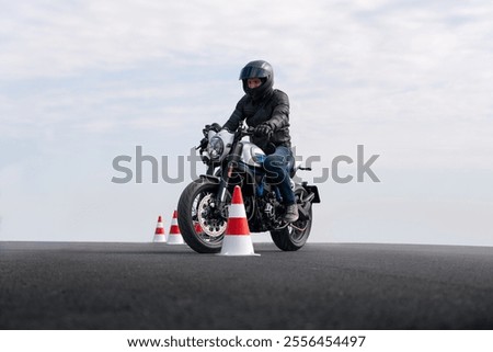 Motorcyclist in full gear practicing precision riding and slalom between traffic cones on an asphalt training ground.