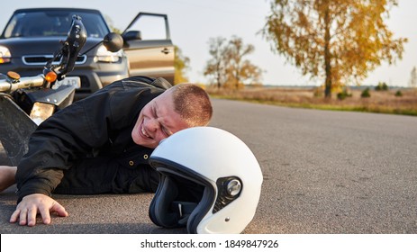 A Motorcyclist Lies On The Asphalt Near A Motorcycle And Car, The Theme Of Road Accidents.