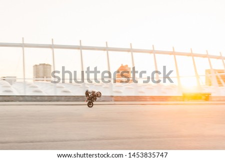 Motorcyclist makes a dangerous trick on the background of the sunset, riding on the rear wheel.Man rides a motorcycle on the background of a beautiful city landscape.Stuntman trains on a motorcycle.