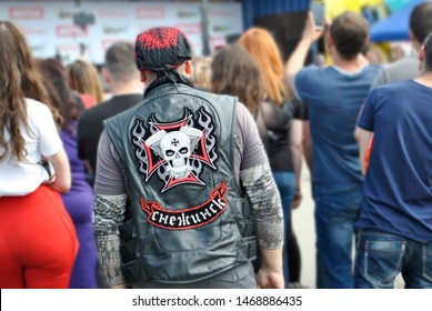 Motorcyclist in a motorcycle suit with a bandana on his head looking at the scene in a crowd of people. On the back of the biker painted skull. All people look in the same direction.