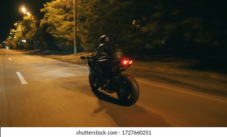 Motorcyclist Racing His Motorcycle On Evening City. Man Riding On Modern Sport Motorbike At Night Street Of Town. Guy Driving Bike During Trip. Concept Of Freedom And Adventure. Rear View Close Up.