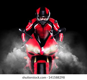 Motorcyclist In Red Equipment And Helmet Riding Motorbike With Headlights On  Over Black Background