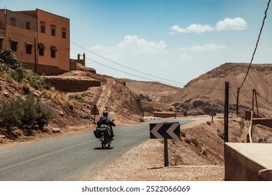 Motorcyclist Riding Along a Winding Road Through the Mountainous Terrain of Morocco on a Sunny Day - Powered by Shutterstock