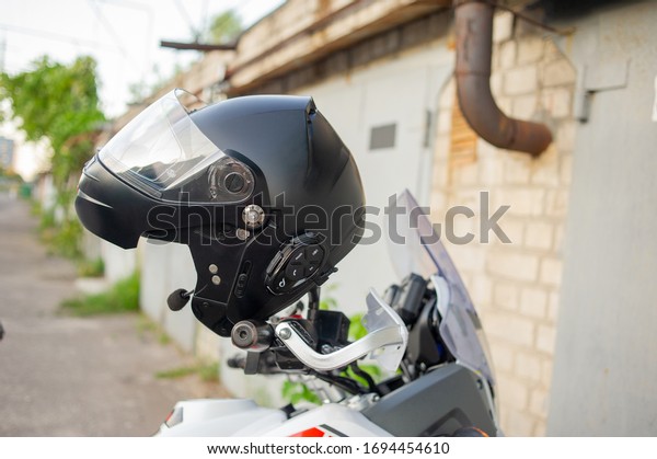 Motorcyclist\'s crash-helmet hanging on the\
handle of a motorcycle. Helmet hanging on the steering wheel on a\
motorcycle. Biker and motorcycle\
concept.