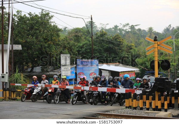 Motorcyclists are stopping behind railroad safety\
bars when a train is about to pass.Purwokerto, Banyumas, Central\
Java,Indonesia. December 7,\
2019.
