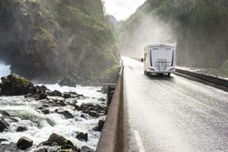 Motorhome Camper Van Driving Fast On Wet Canyon Valley Road And Bridge Across Waterfall River. Norway.