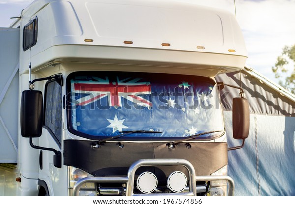 Motorhome campervan with flag of Australia on the\
windscreen at the campground. Australian camping, tourism and\
travel lifestyle\
concept