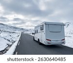A motorhome driving along the Sognefjellsvegen road in south Norway, surrounded by snow-covered mountains and scenic views.