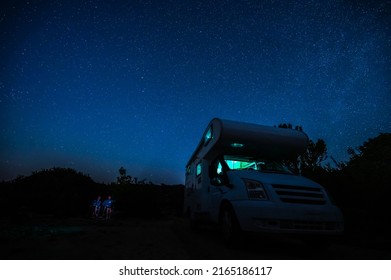 Motorhome RV Parked Under Stars On A Pier By The Sea, Crete, Greece. Travelers With Camper Van Are Resting Overnight Under Milky Way On An Active Family Vacation, Crete, Greece.