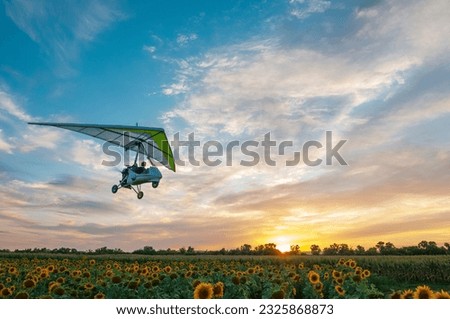 Motorized hang glider trike plane flies low above beautiful sunflower field at the sunset