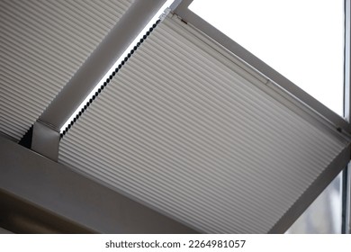 Motorized pleated blinds on the roof windows. Blinds for skylights, beige color. Honeycomb pleated curtains on glass roof.