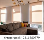 Motorized roller blinds. A sofa with colorful pillows in the room near windows with sunscreen curtain. Automatic roller shades on full height windows in the interior. Sunny day. Selective fokus.