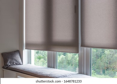 Motorized roller shades. Automatic roller blinds beige color on large windows. Remote Control Shades are near the sofa with the pillow. Sofa covered with pastel velours. Summer. Green trees outside. - Shutterstock ID 1648781233