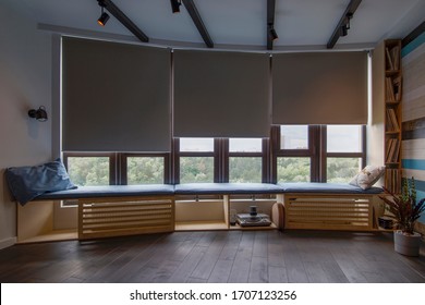 Motorized roller shades in the interior. Automatic roller blinds beige color on big glass windows. Remote Control Shades are above the windosill with pillows. Summer. Green trees outside. - Shutterstock ID 1707123256