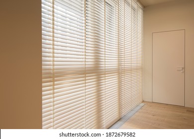 Motorized Wood Blinds In The Interior. Automatic Venetian Blinds Beige Color On Large Windows. Wooden Slats 50mm Wide. A Door To The Room Is Near The Window. 