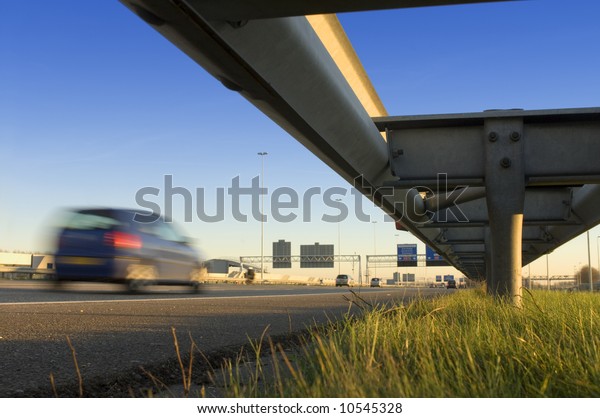A motorway safety rail with route\
information sign and motion blurred passing\
cars