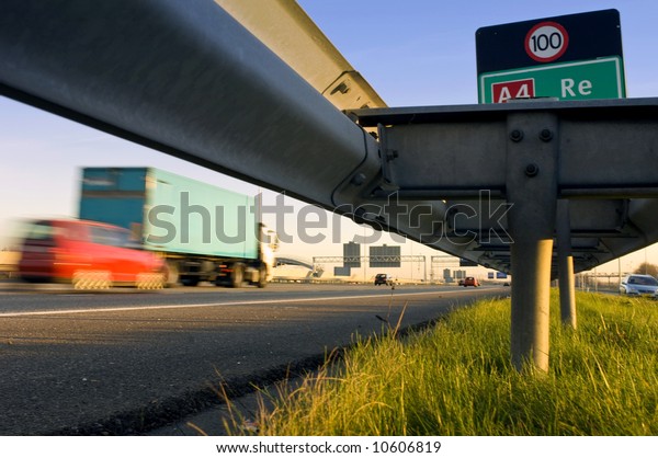 A motorway safety rail with route\
information sign and motion blurred passing\
cars