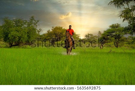 A Motswana man from Botswana riding a horse on the wetlands, at sunset, 