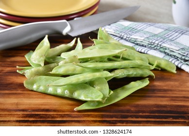 A Mound Of Fresh, Uncookes Snow Peas On A Cutting Board