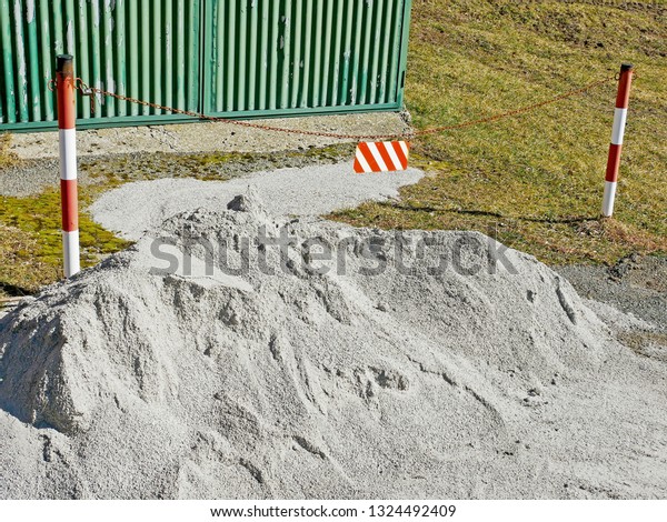 A mound of sand from a\
construction site along a country road with a work shed and tool\
shed.