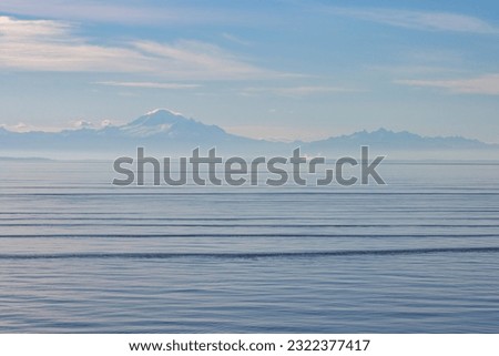 Mount Baker on a hazy summer morning from the ferry on the strait of juan de fuca. Blue skies with wispy clouds and small waves.