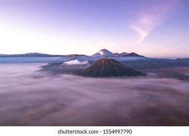 Mount Bromo at sunrise; Island of East Java, Indonesia. Clouds blanket the valley; gas escaping from the crater. Flames and lava can be seen on the volcanic peak in the background.
