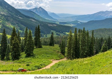 Mount Crested Butte - A red SUV running down a winding mountain road in a green valley towards Mount Crested Butte on a sunny Summer morning. Crested Butte, Colorado, USA. - Shutterstock ID 2126125625