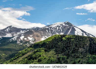 Mount Crested Butte Snow Mountain During Sunset In Summer With Green Lush Color On Hills And Forest