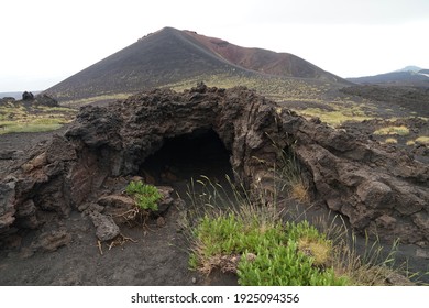 Mount Etna volcanic landscape with hidden cave on side crater with ash, stones and green patches of scrub, guided hiking tour on Etna, Sicily, Italy