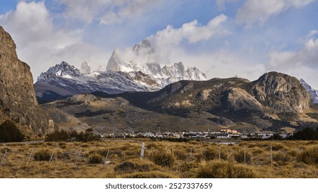           Mount Fitz Roy in Patagonia, Argentina, with its snow-capped peaks towering above the small town of El Chaltén, framed by rugged hills and dramatic skies.                      - Powered by Shutterstock