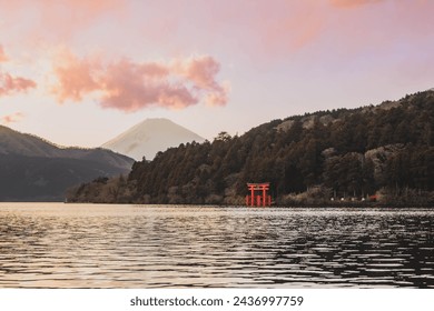 Mount Fuji, Lake Ashi in Hakone, Japan, featuring the iconic red Torii Gate. The soft pink hues of sunset illuminate the sky, with Fuji San's peak visible in the evening light with copy space.  - Powered by Shutterstock
