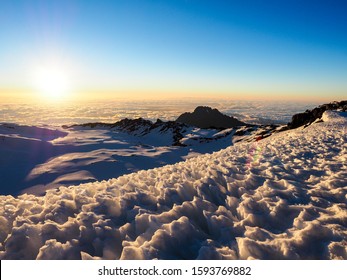 Mount Kilimanjaro And Meru In The Tanzanian Serengiti As Dawn Breaks Above The Clouds. Hikers Make The Slow Trek To The Summit For Sunrise