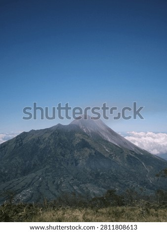 Mount merapi in indonesia, an active stratovolcano with green slopes and rugged peaks under a blue sky with clouds. Ideal for travel websites and geological studies.