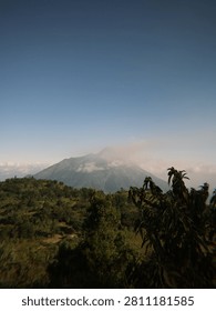 Mount merapi volcano in a hazy, cloudcovered sky with green leaves, creating a stunning natural landscape. Perfect for environmental and travel designs.